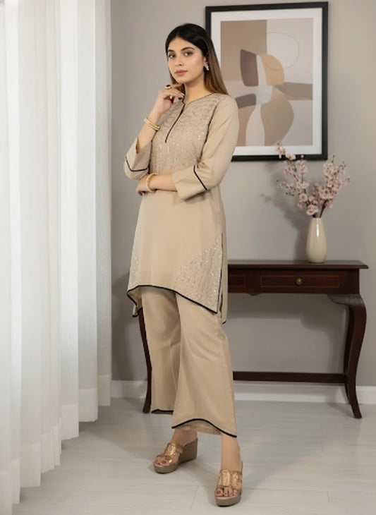 Woman in a beige traditional outfit standing in a room with a decorative wall piece and table.