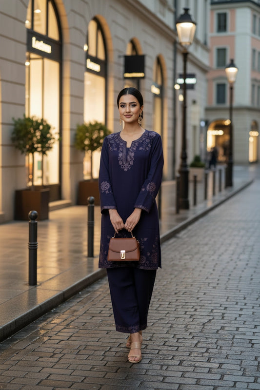 Woman in a dark blue embroidered dress standing on a cobbled street with shops in the background