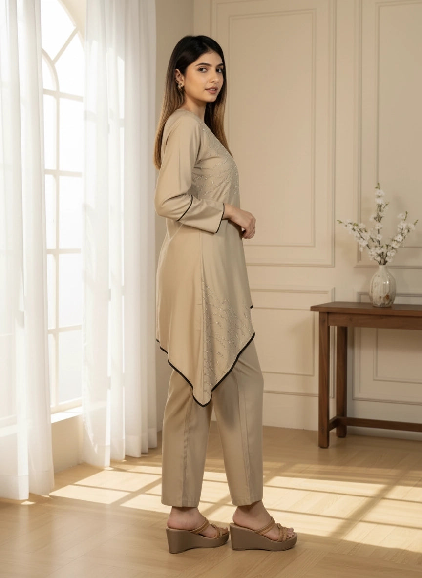 Woman in beige outfit standing in a well-lit room with a wooden table and decorative plant.