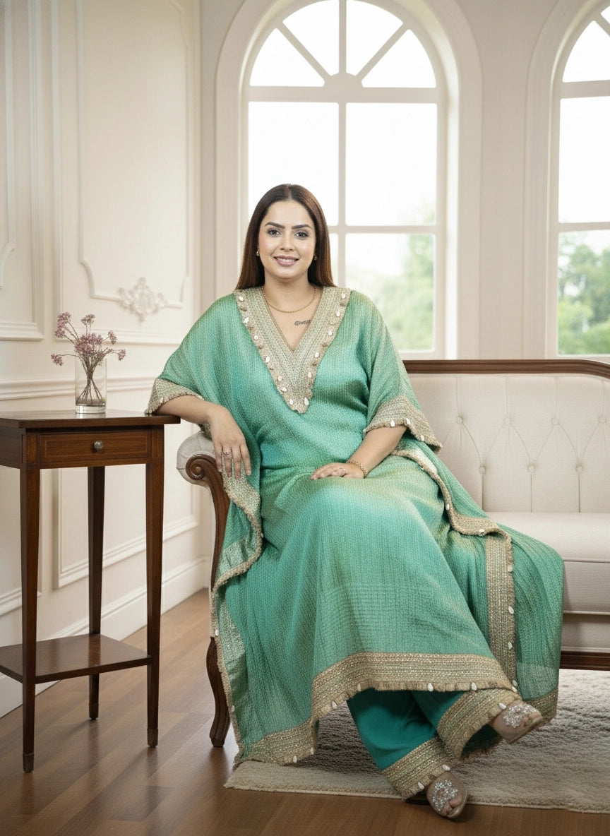 Woman in a light green saree sitting in a well-lit room with large windows.