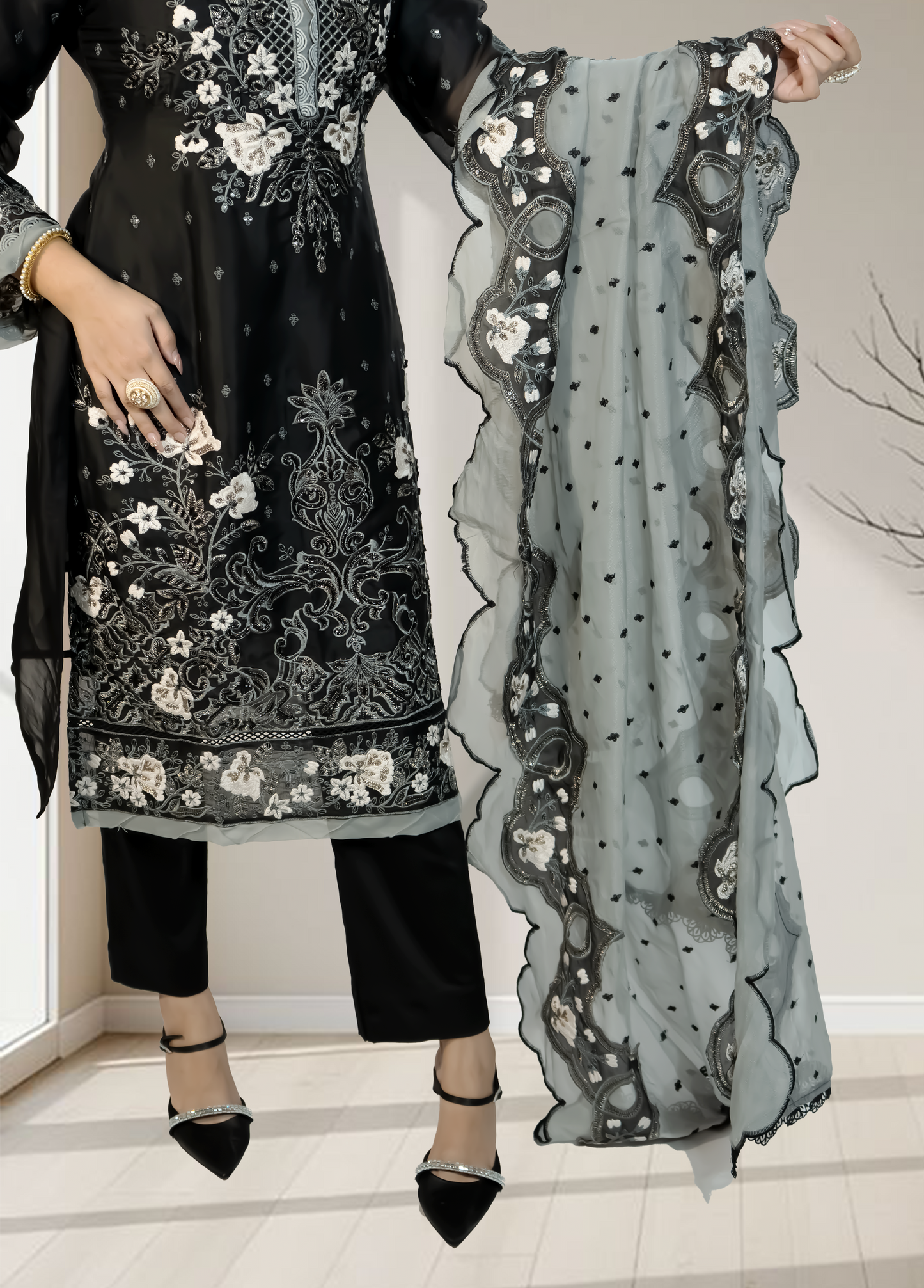 Black embroidered outfit with a sheer gray scarf held by a person indoors.