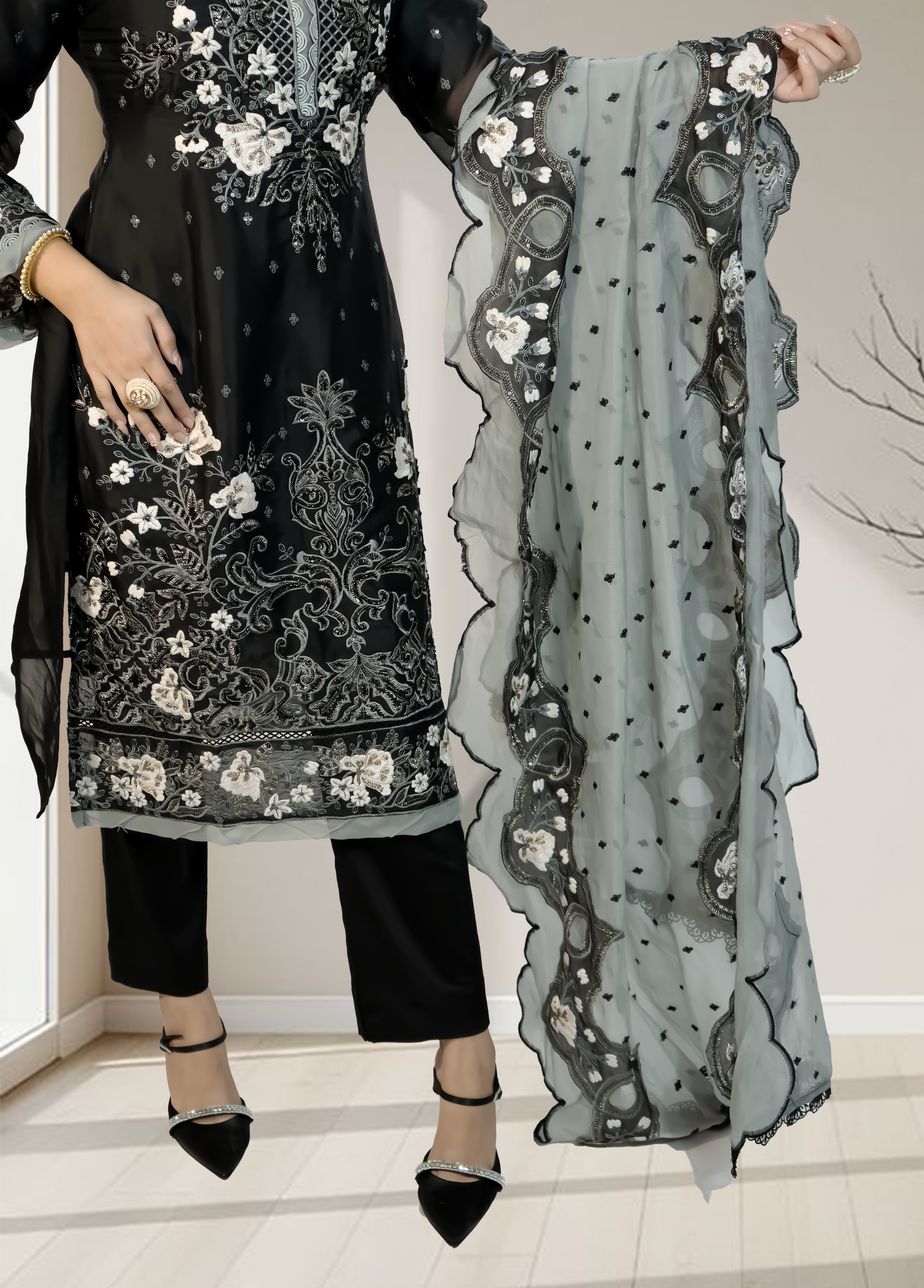 Black embroidered outfit with a sheer gray scarf held by a person indoors.