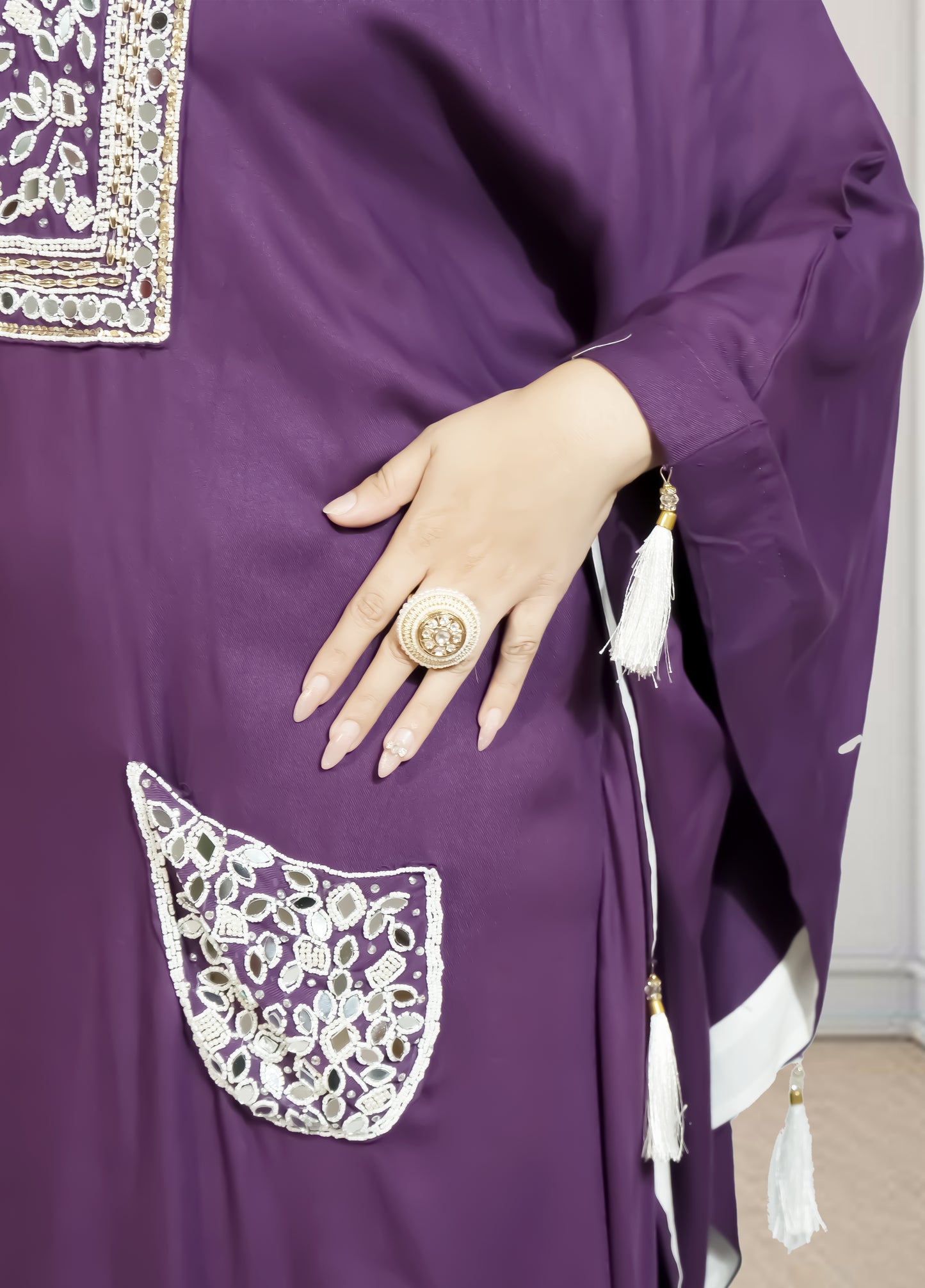 Purple garment with white embroidery and a hand wearing a ring, on a neutral background