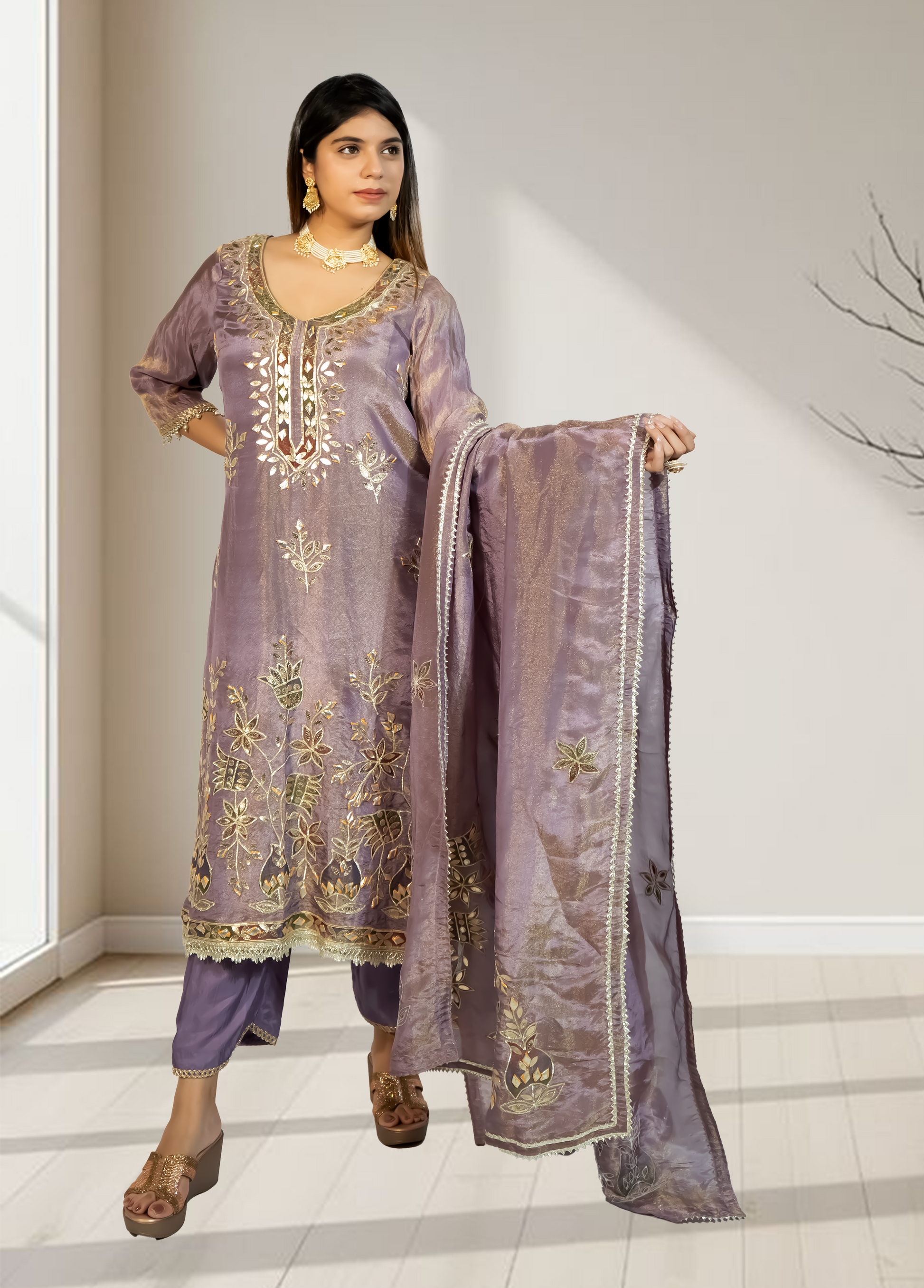 Woman wearing a traditional embroidered outfit with a matching dupatta in a well-lit room.