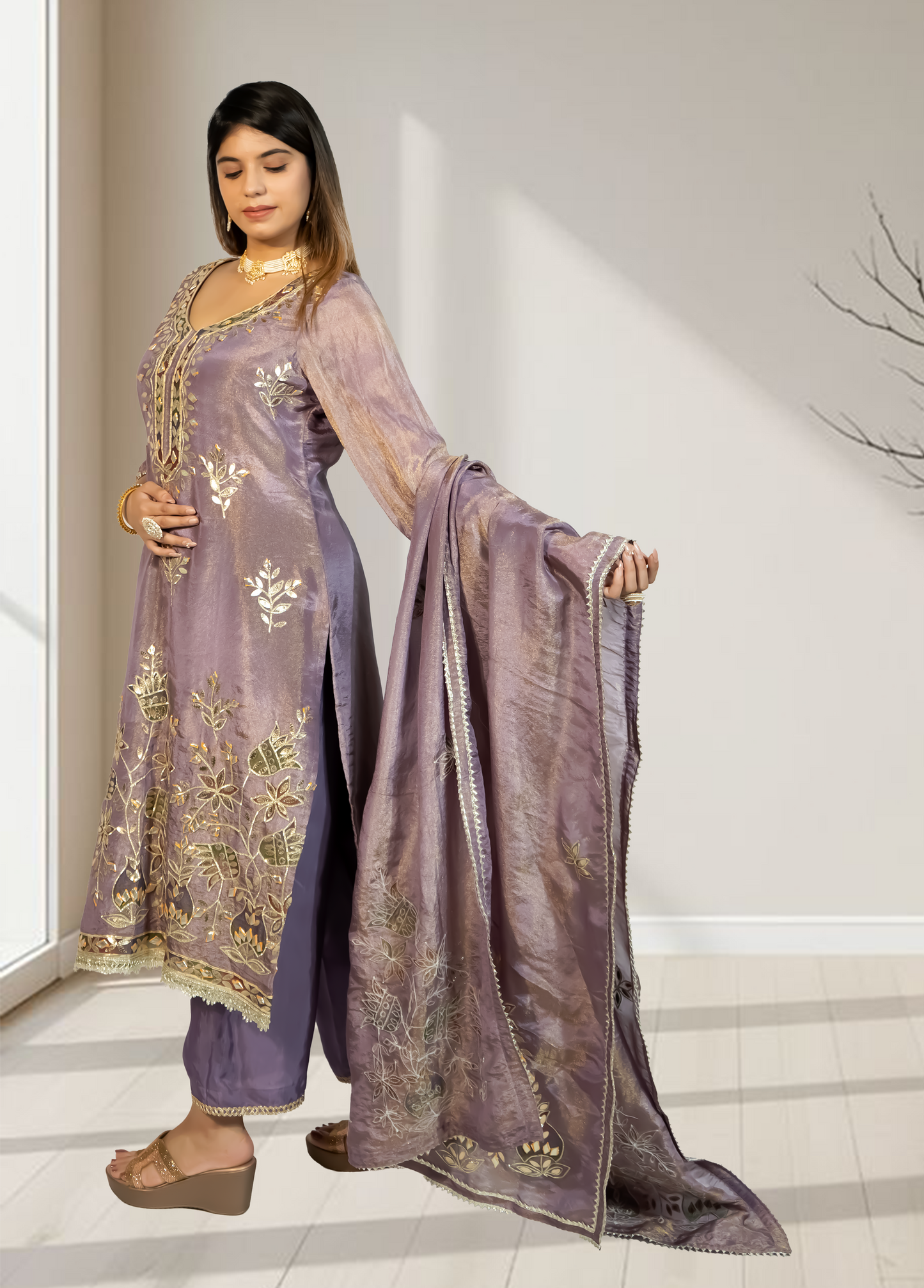 Woman wearing a traditional outfit with a purple dupatta in a well-lit room.