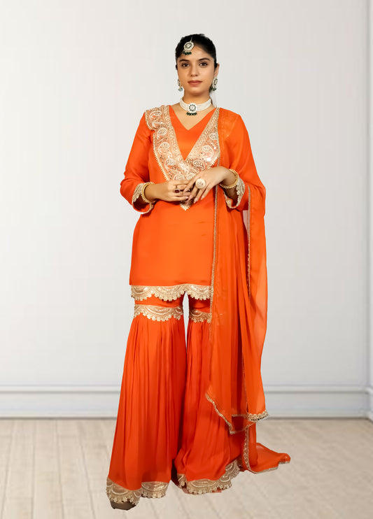 Woman wearing an orange traditional outfit with gold embroidery against a white background