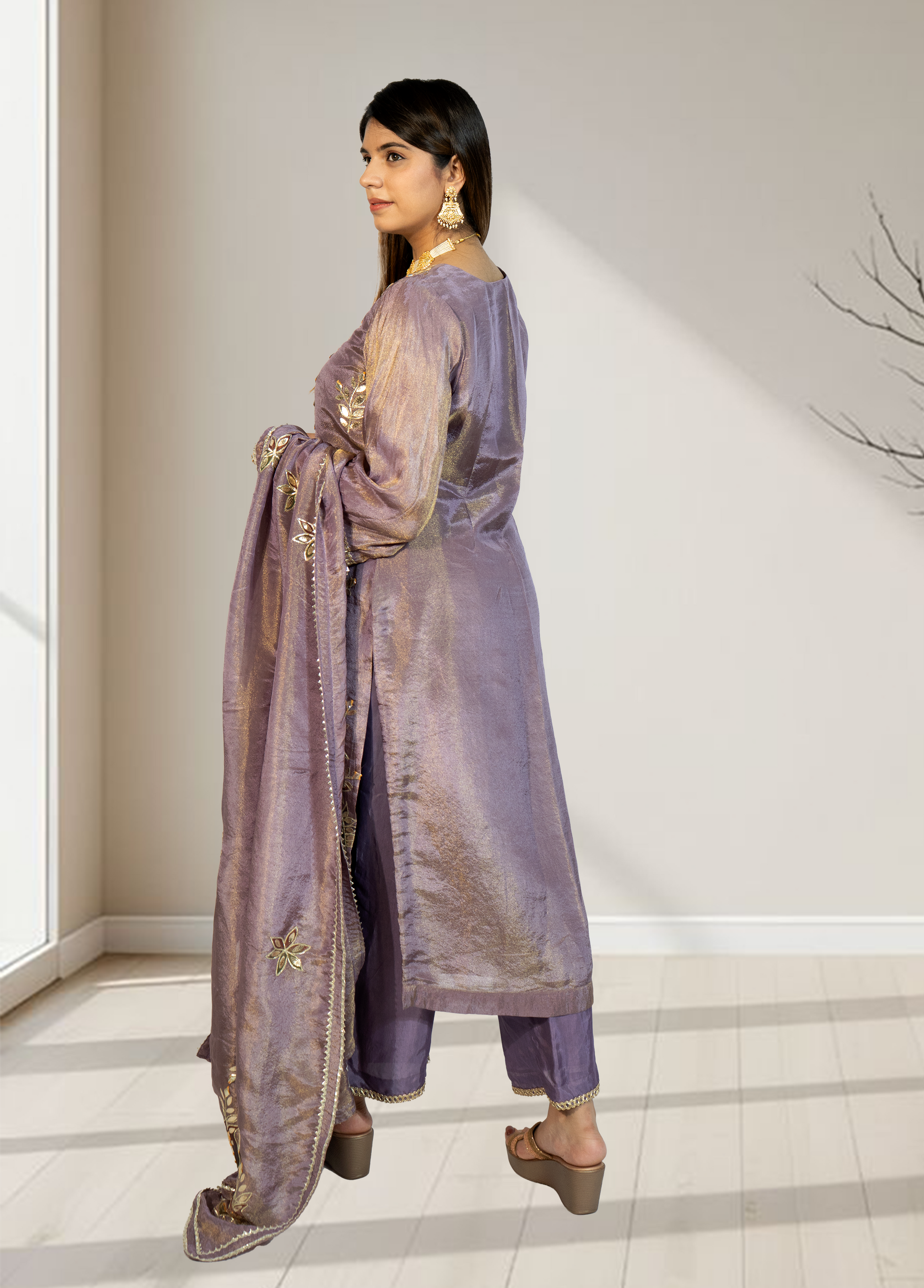 Woman wearing a traditional outfit with a long purple dupatta in a minimal indoor setting