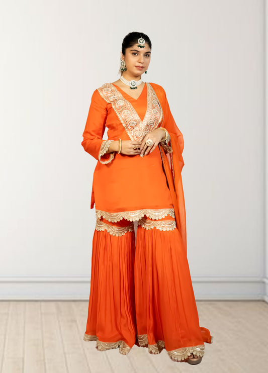 Woman wearing an orange traditional outfit with white embroidery on a plain background