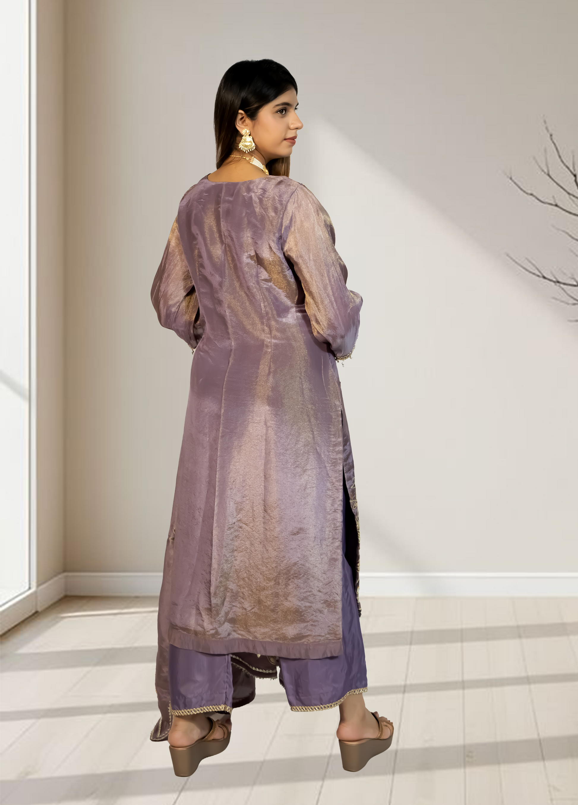 Woman wearing a long, light purple dress with a sheer overlay in a minimal indoor setting.