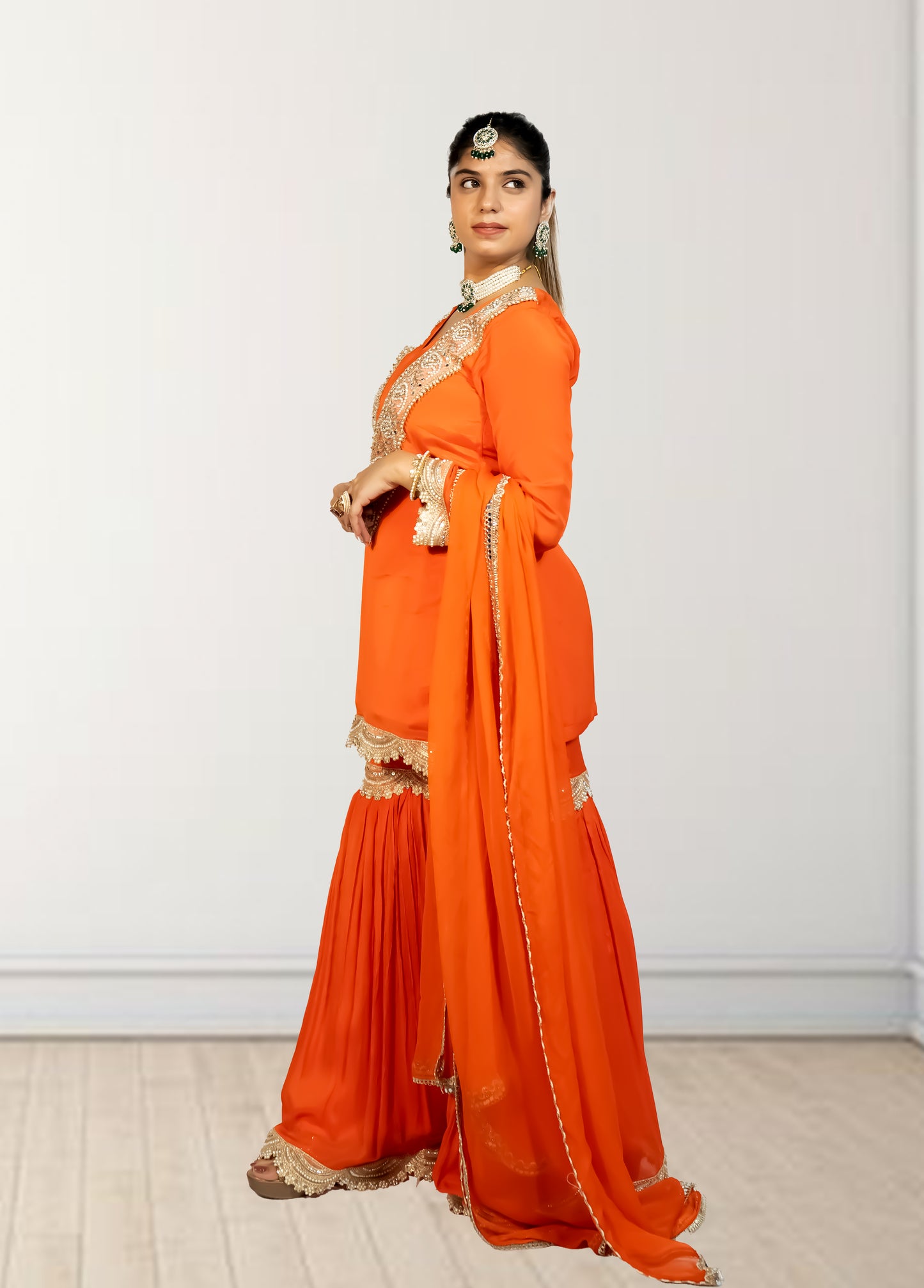 Woman wearing an orange saree with gold border on a white background