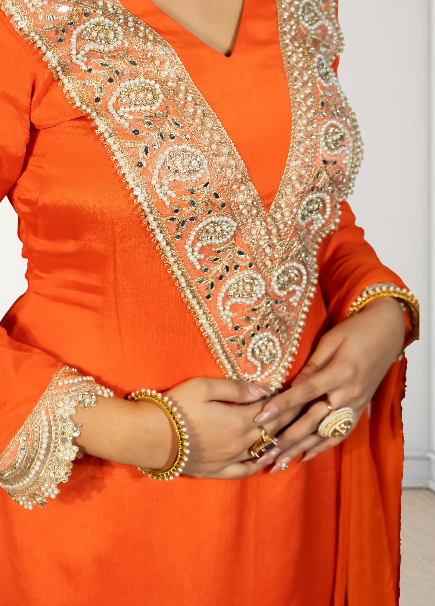 Orange traditional outfit with intricate gold embroidery on a plain background