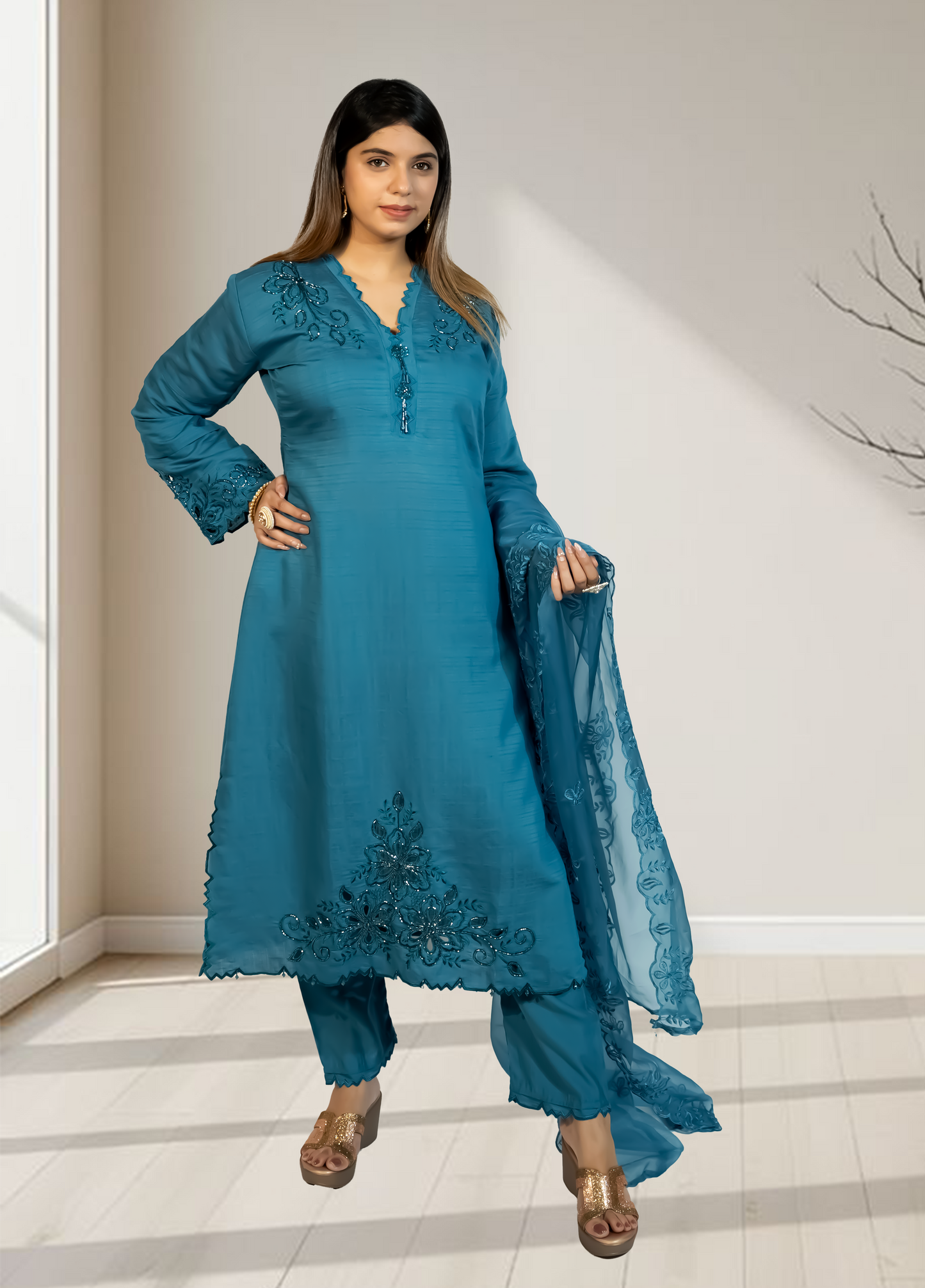 Woman wearing a teal embroidered outfit with a matching dupatta in a well-lit room.