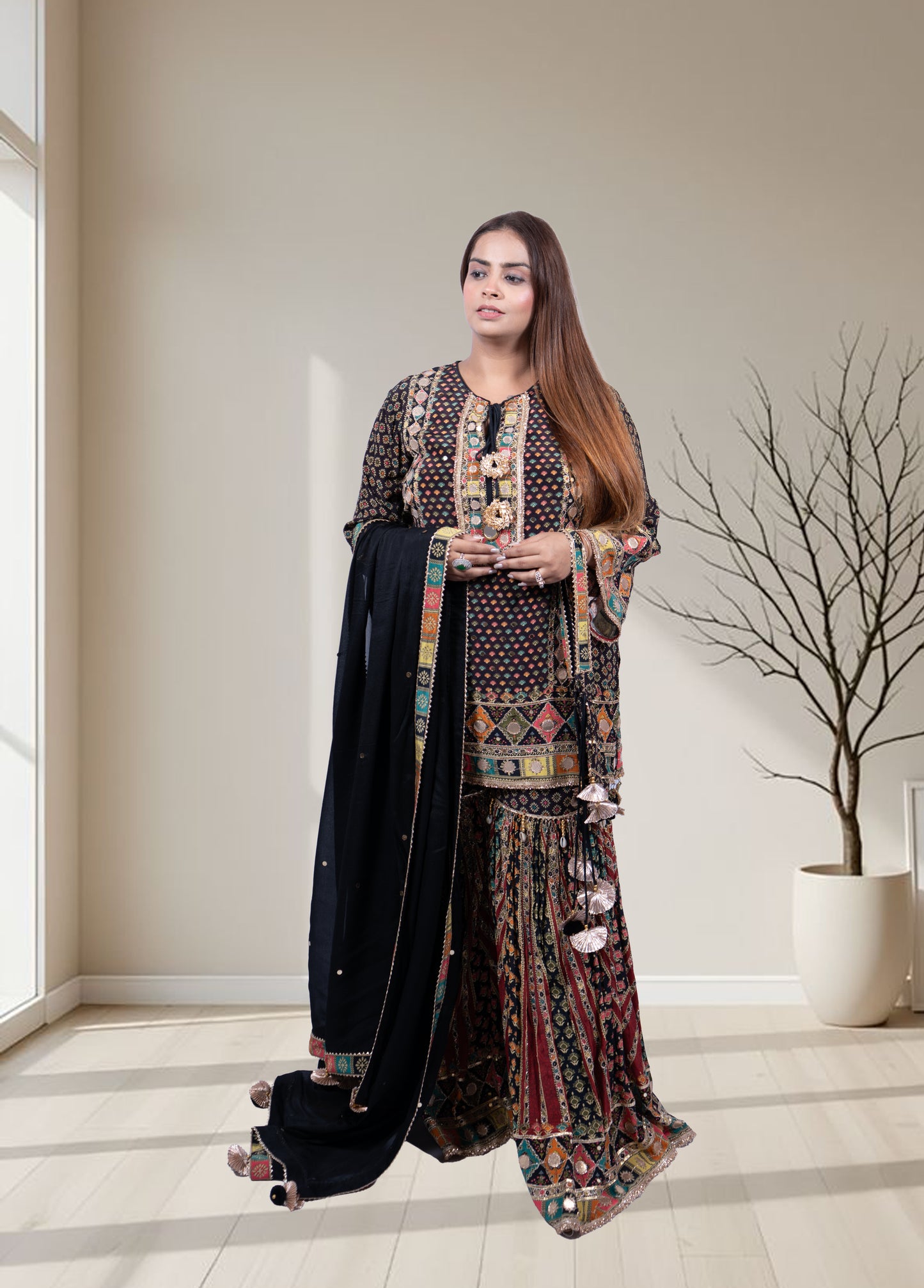 Woman in a patterned outfit standing in a room with a large window and decorative plant.