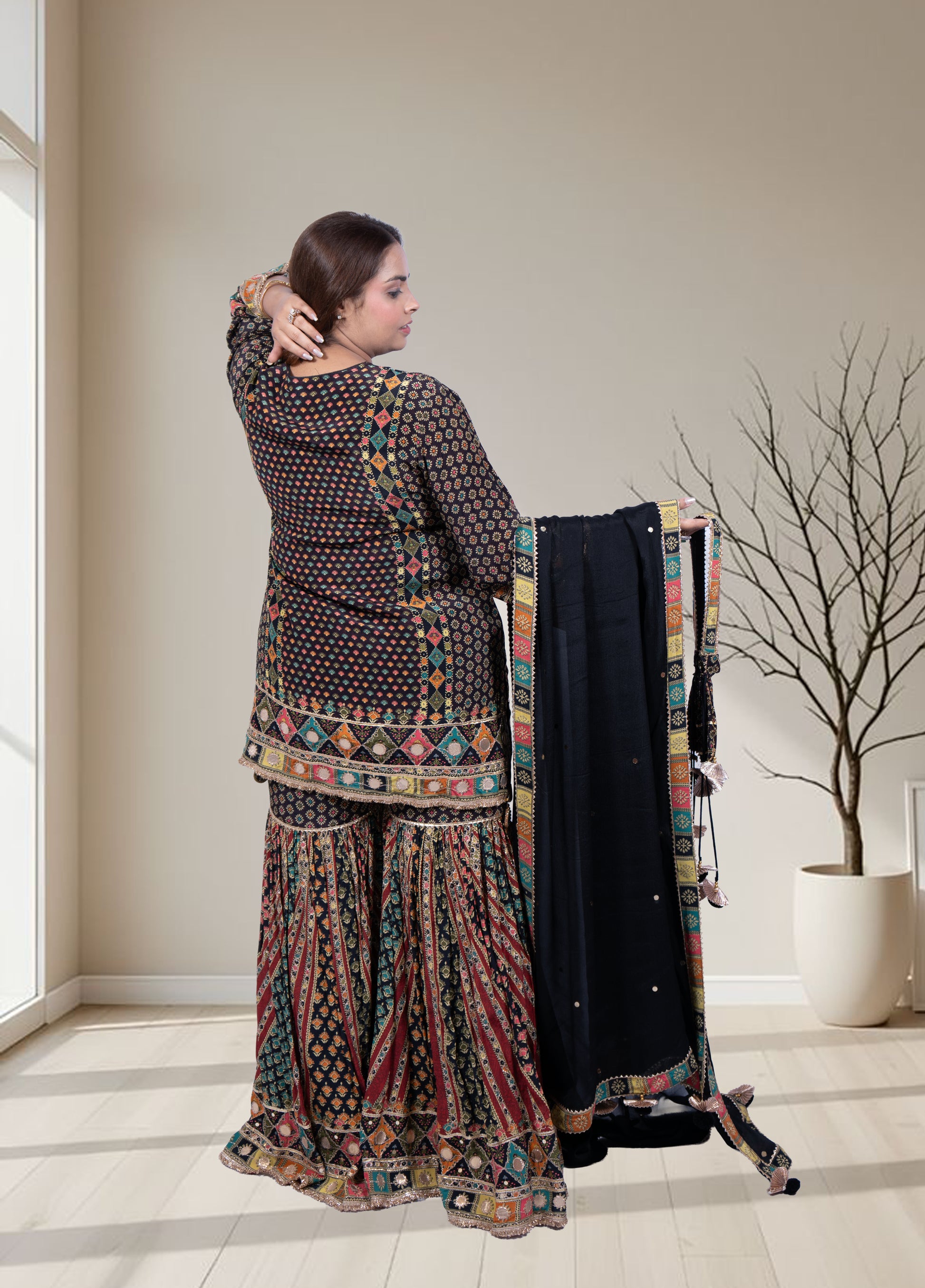 Woman in traditional outfit holding a garment in a room with a window and plant.