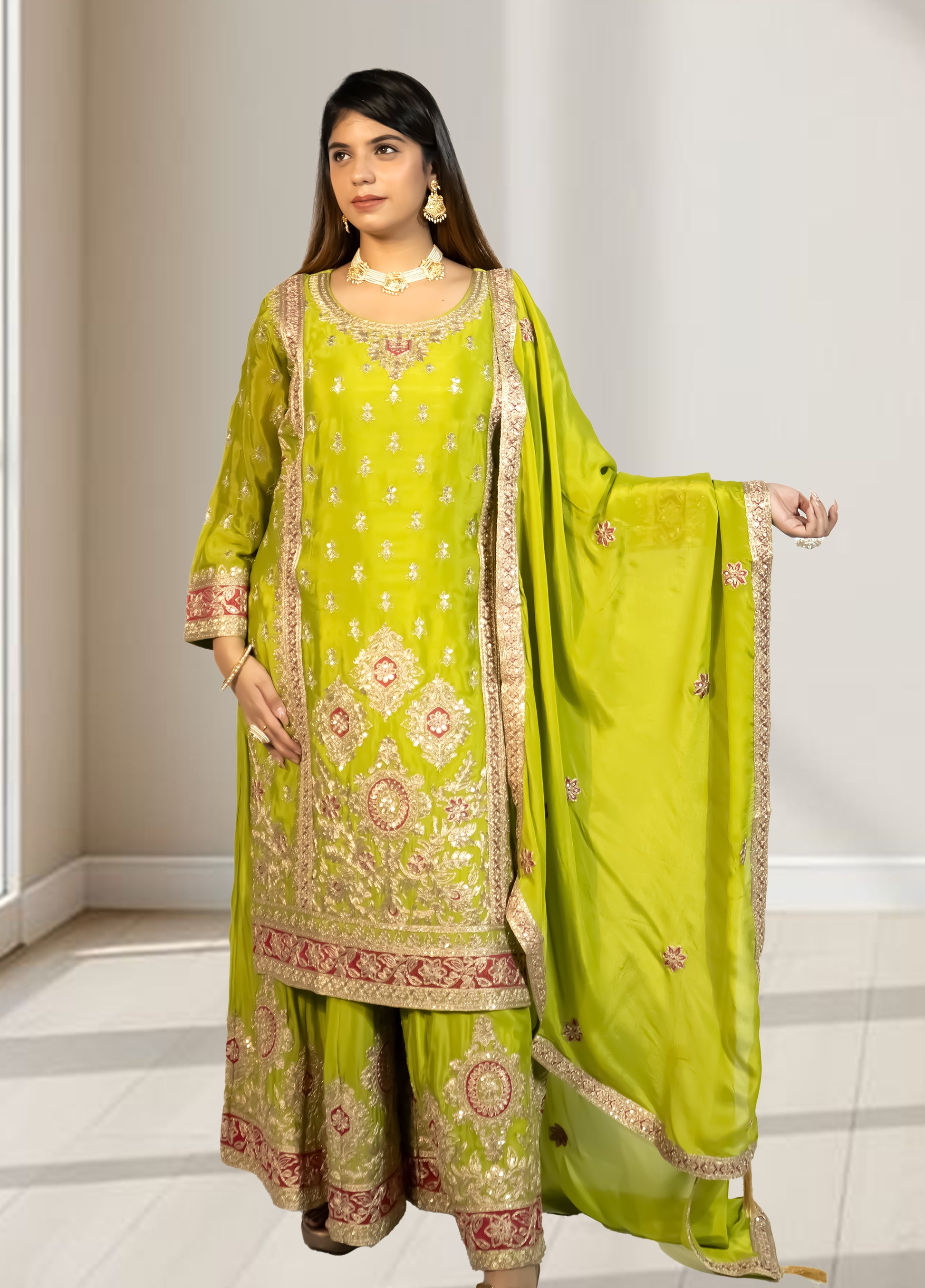 Woman wearing a green embroidered traditional outfit with a matching dupatta in a well-lit room.
