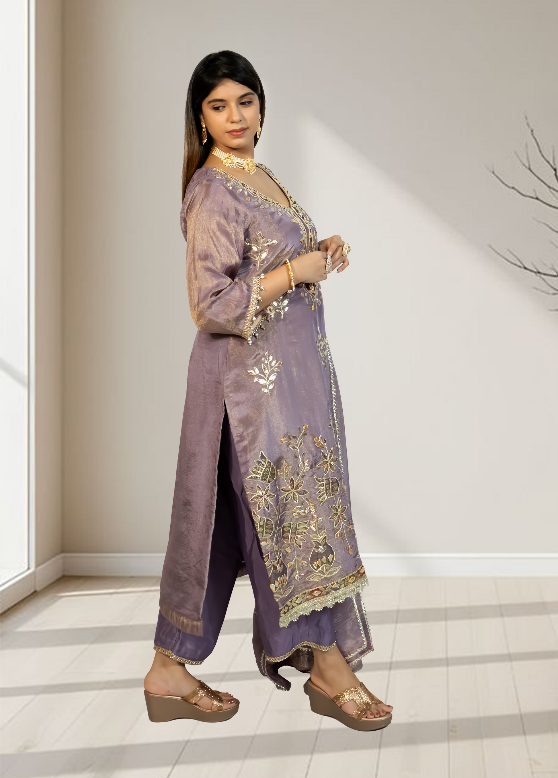 Woman wearing a traditional embroidered outfit in a room with large windows.