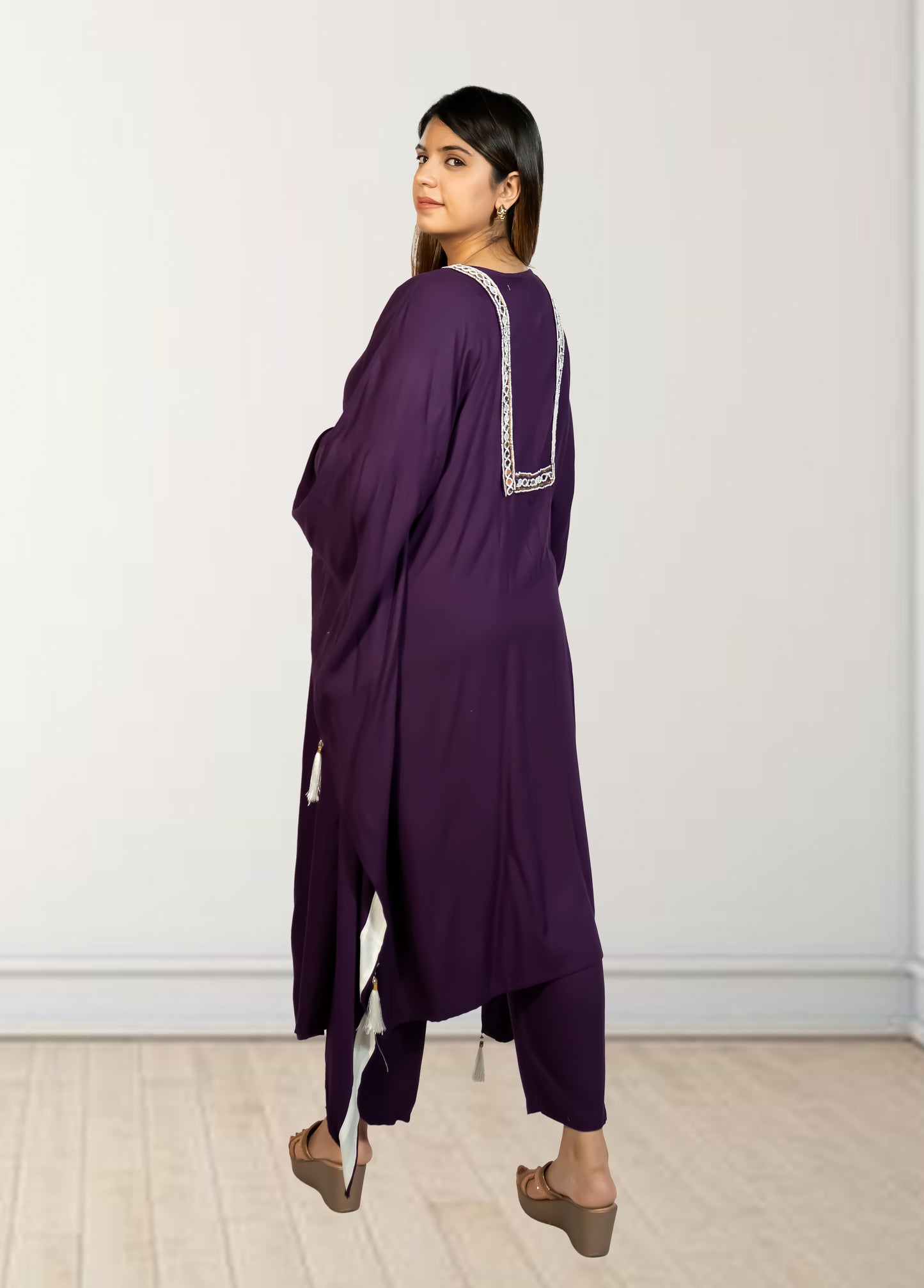Woman wearing a purple outfit with white embroidery against a white wall.