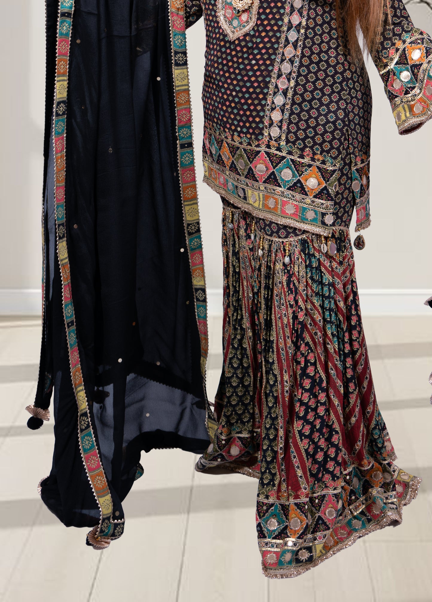 Traditional outfit with a patterned top and black skirt on a white floor.