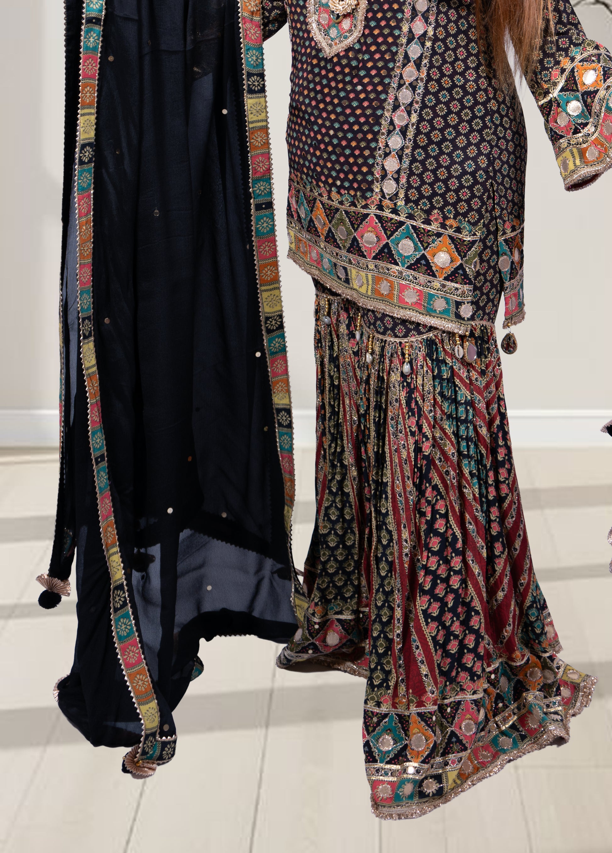 Traditional outfit with a patterned top and black skirt on a white floor.