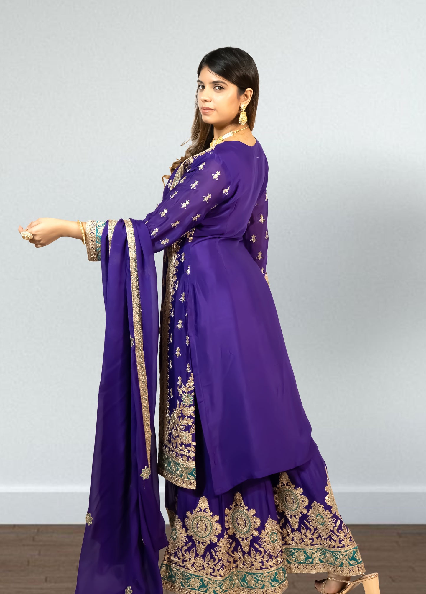 Woman wearing a purple traditional outfit with gold embroidery on a plain background