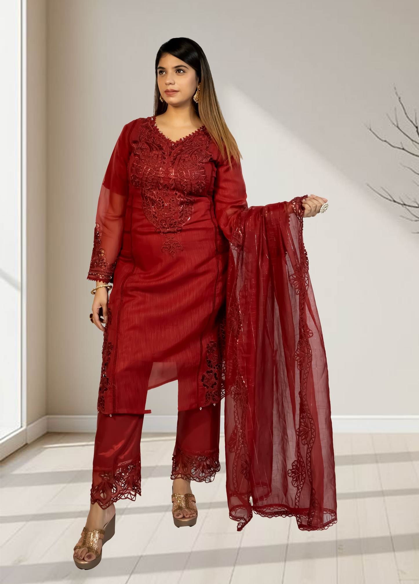 Woman wearing a red traditional outfit with a matching dupatta in a minimalistic setting.