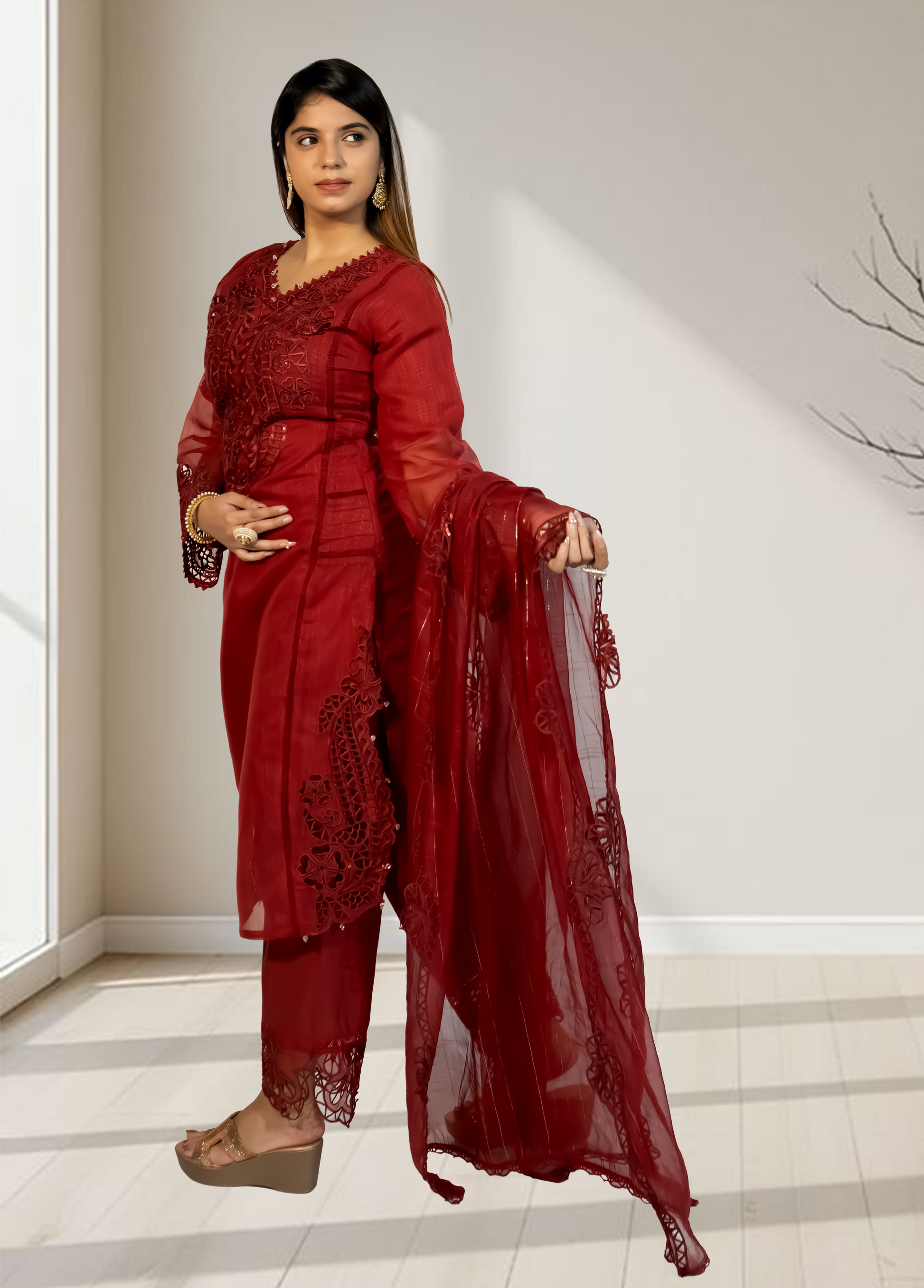 Woman wearing a red traditional outfit with a matching dupatta in a minimal indoor setting.