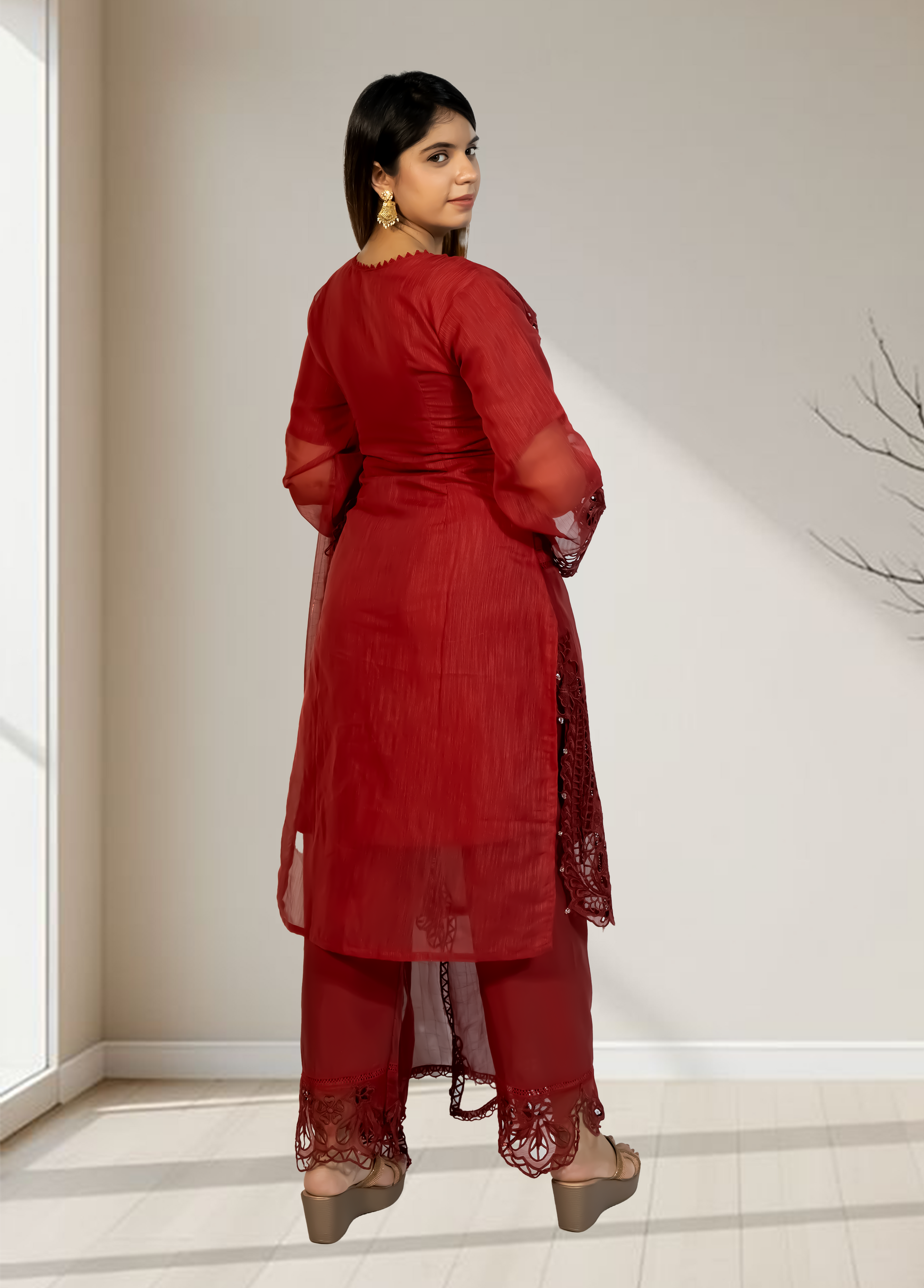 Woman wearing a red traditional outfit standing in a minimalistic room.
