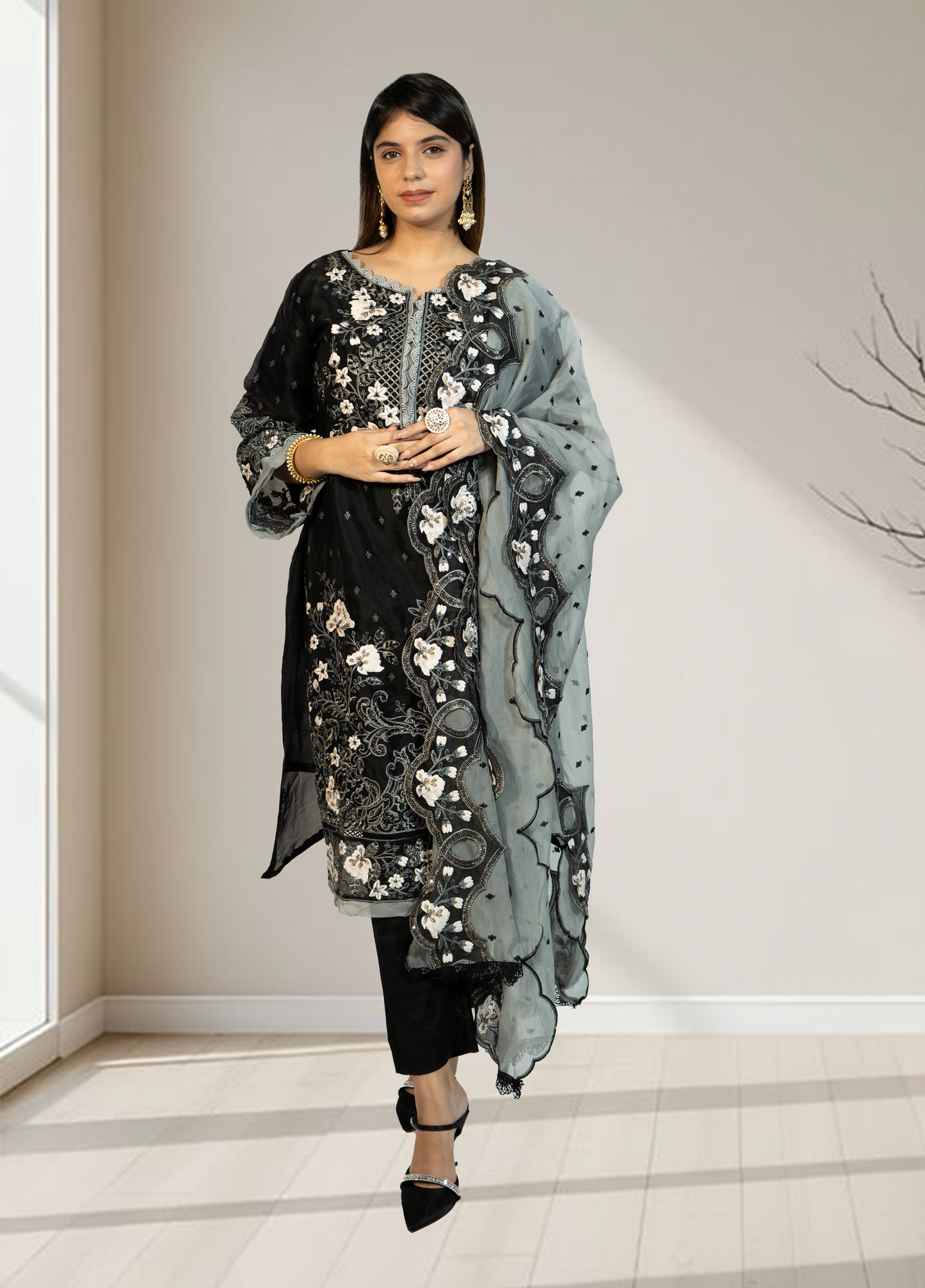 Woman wearing a black floral embroidered outfit with a matching dupatta in a minimal indoor setting.