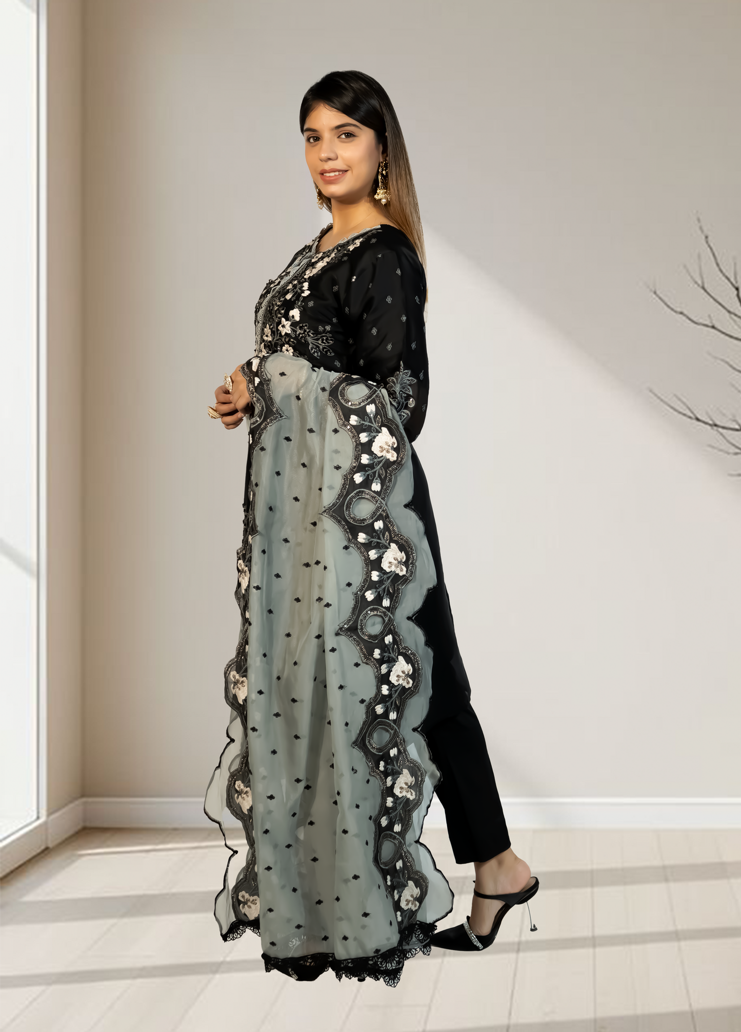 Woman wearing a black outfit with a sheer, embroidered dupatta in an indoor setting