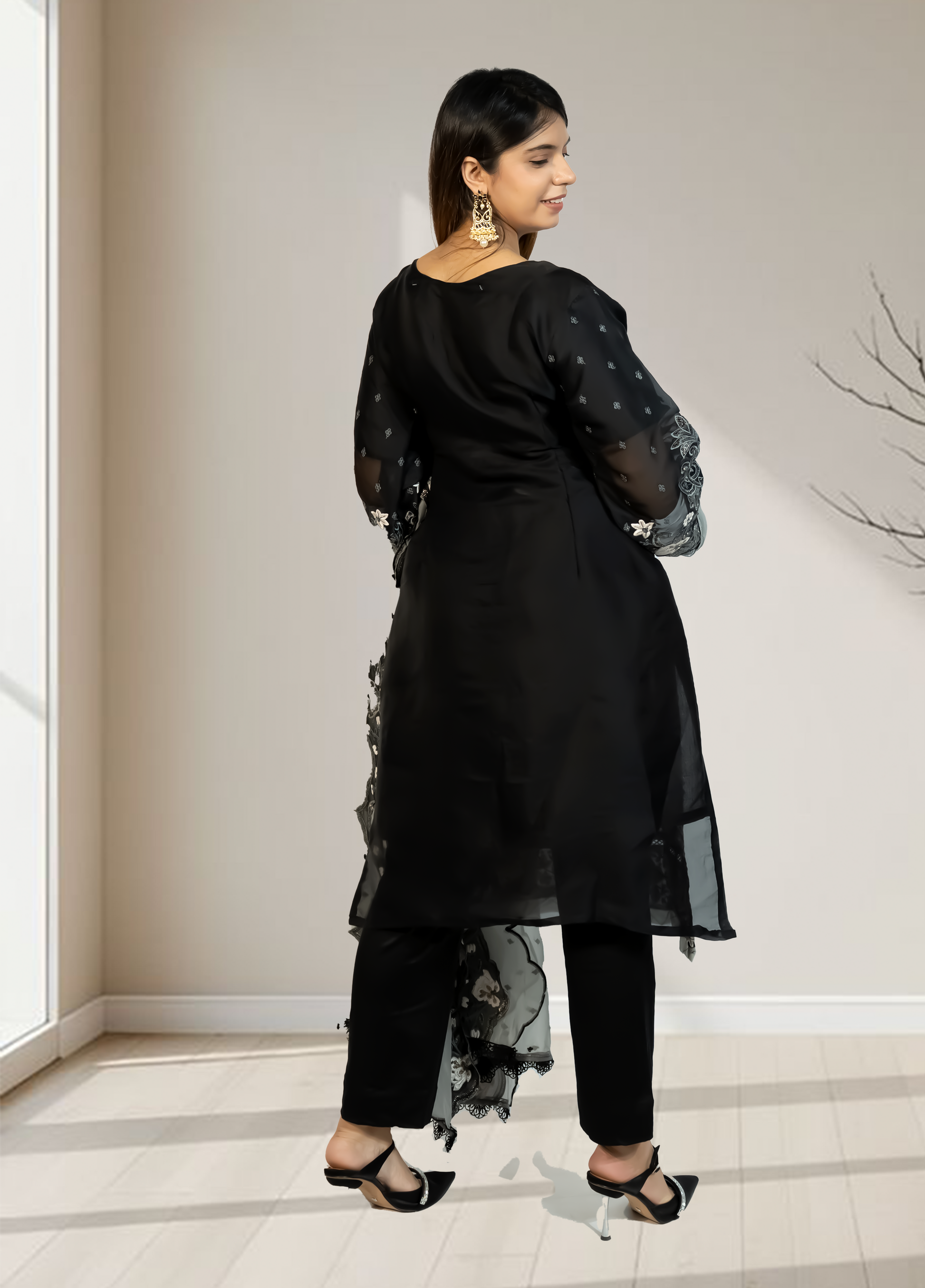 Woman wearing a black outfit with sheer sleeves and bottom hem in a minimal indoor setting