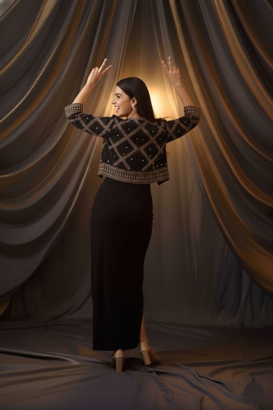 Woman in a black outfit with gold patterns standing in front of draped curtains