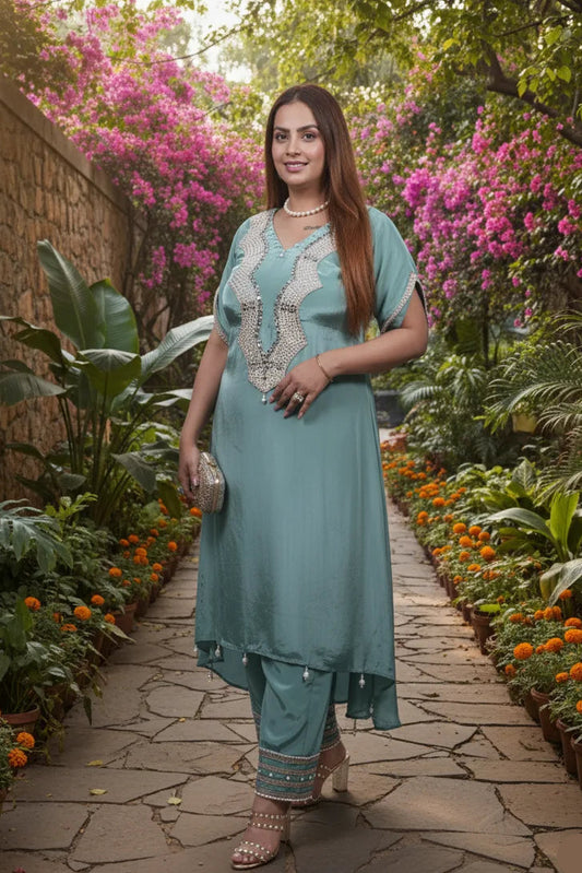 Woman in a teal outfit standing in a garden with flowers and plants.