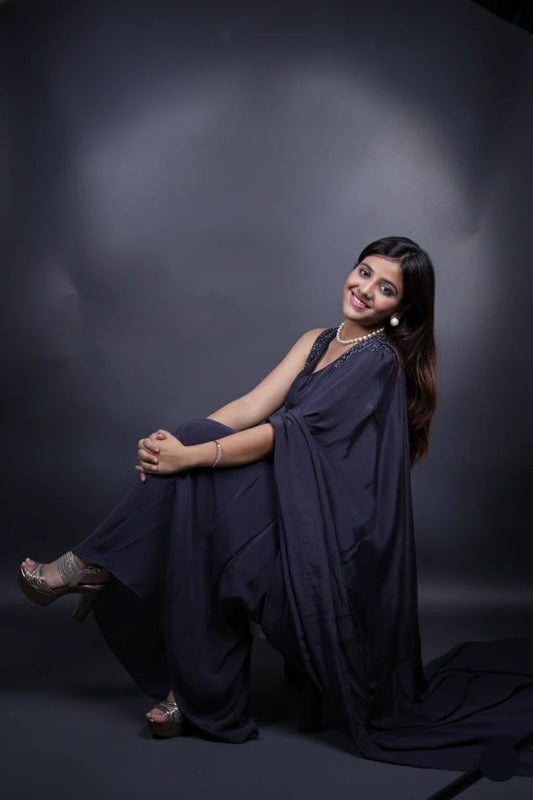 Woman in a dark blue saree sitting against a black background