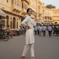 Woman in a white outfit standing on a street with traditional architecture in the background