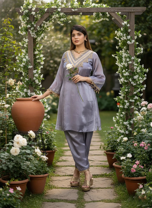 Woman in a light purple outfit standing in a garden with floral arches and potted plants.