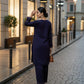 Woman in a navy blue outfit walking on a city street at dusk.