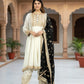 Woman in traditional outfit standing in a decorative indoor setting with arches and plants.