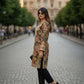 Woman in a patterned coat walking on a city street with classical architecture in the background