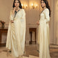 Woman in a cream suit with intricate designs in a elegant indoor setting.