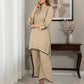 Woman in a beige traditional outfit standing in a room with a decorative wall piece and table.