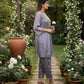 Woman in a gray outfit standing under a floral archway in a garden.