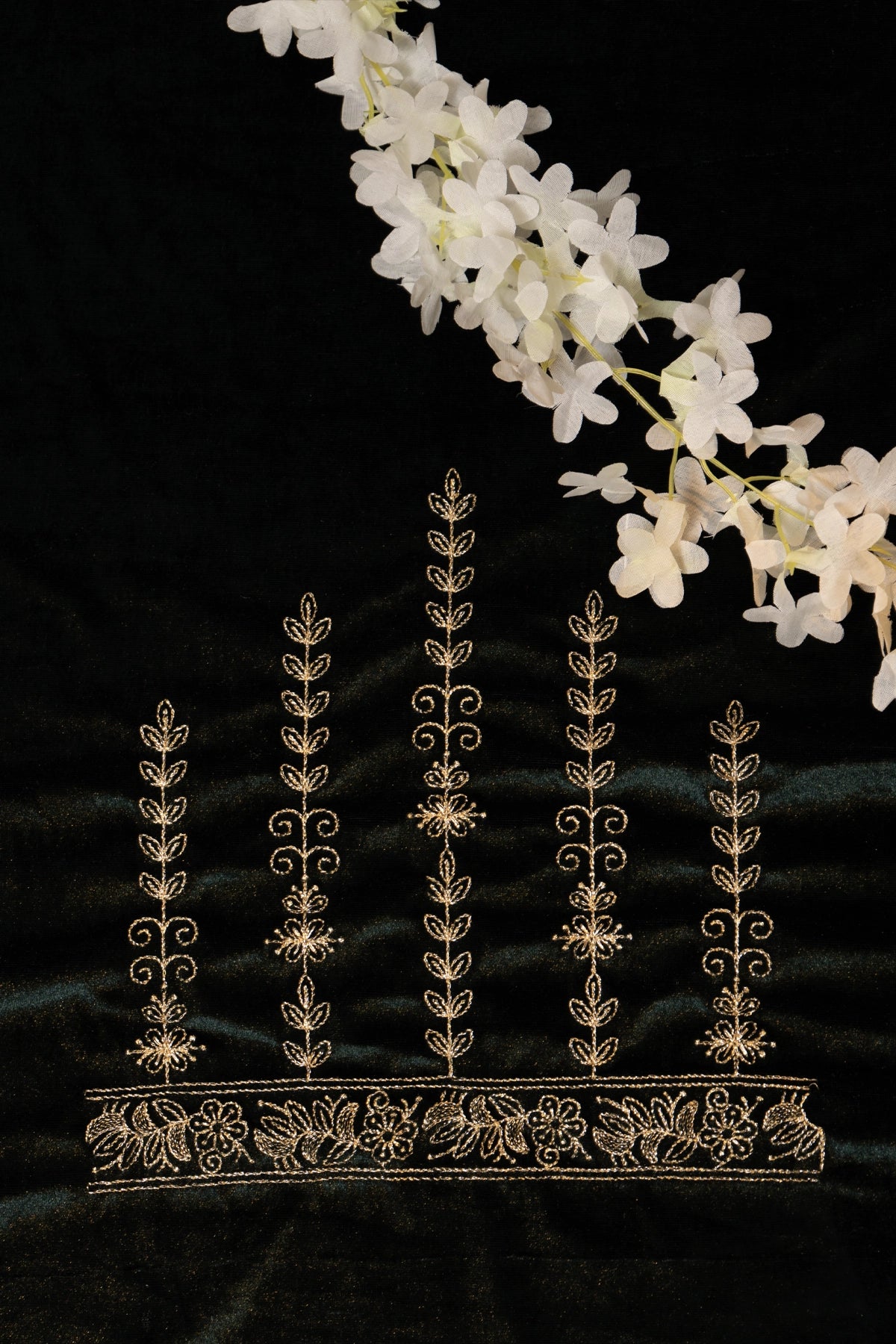 Decorative gold lace on a black background with white flowers.
