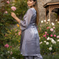 Woman in a light gray outfit standing in a garden with flowers