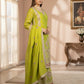 Woman in a green traditional outfit standing in a well-lit room with a painting on the wall.