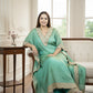 Woman in a light green saree sitting in a well-lit room with large windows.