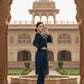Woman in a blue traditional outfit standing in front of an architectural archway with a historical building in the background.