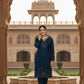 Woman in a navy blue traditional outfit standing in front of an architectural archway with a building in the background.