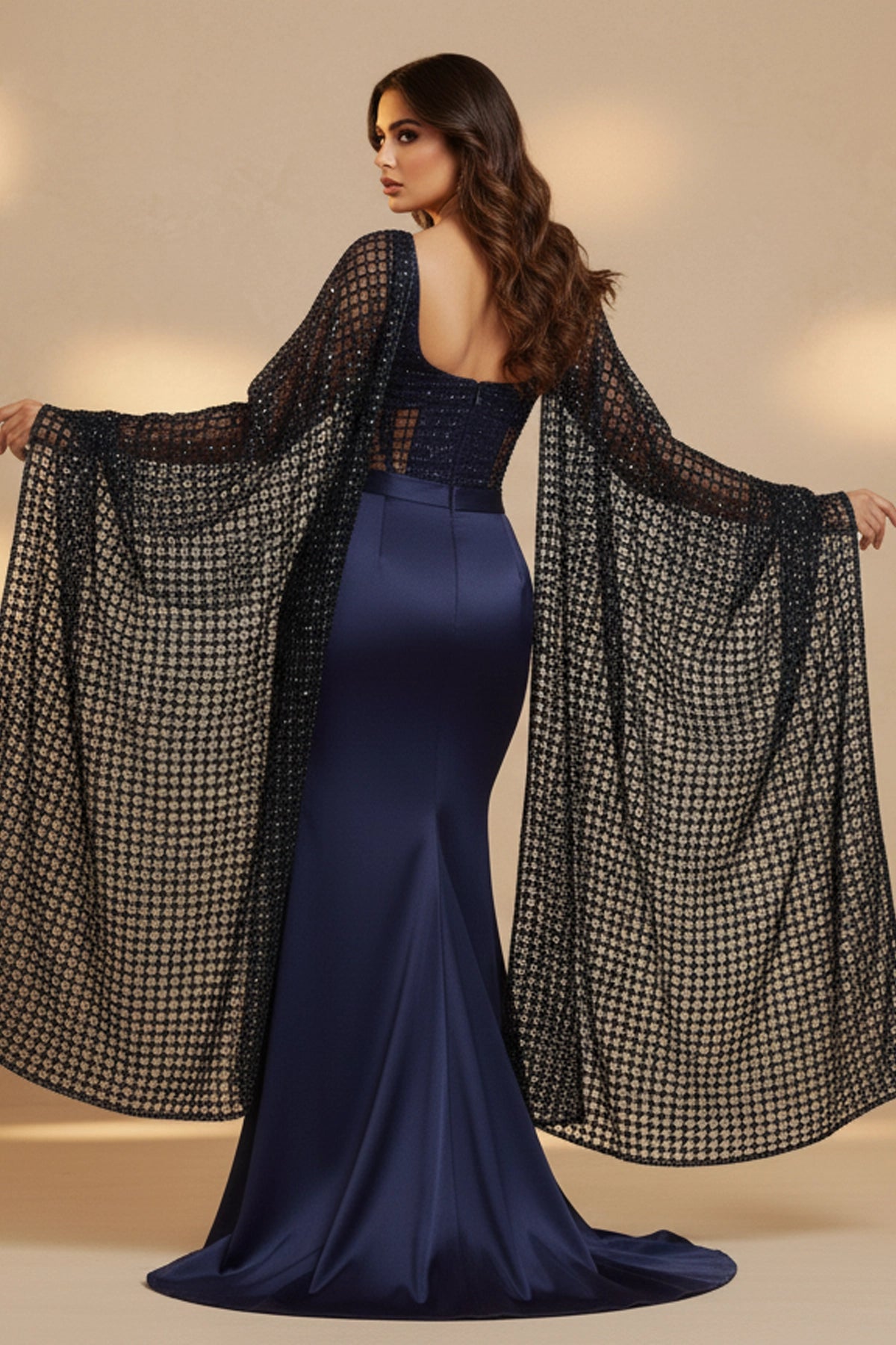 Woman wearing a blue evening gown with a black mesh cover-up on a beige background