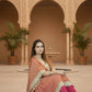 Woman in traditional attire sitting in a decorative indoor setting with arches and plants.