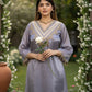 Woman in a light blue embroidered dress holding a white flower in a garden setting